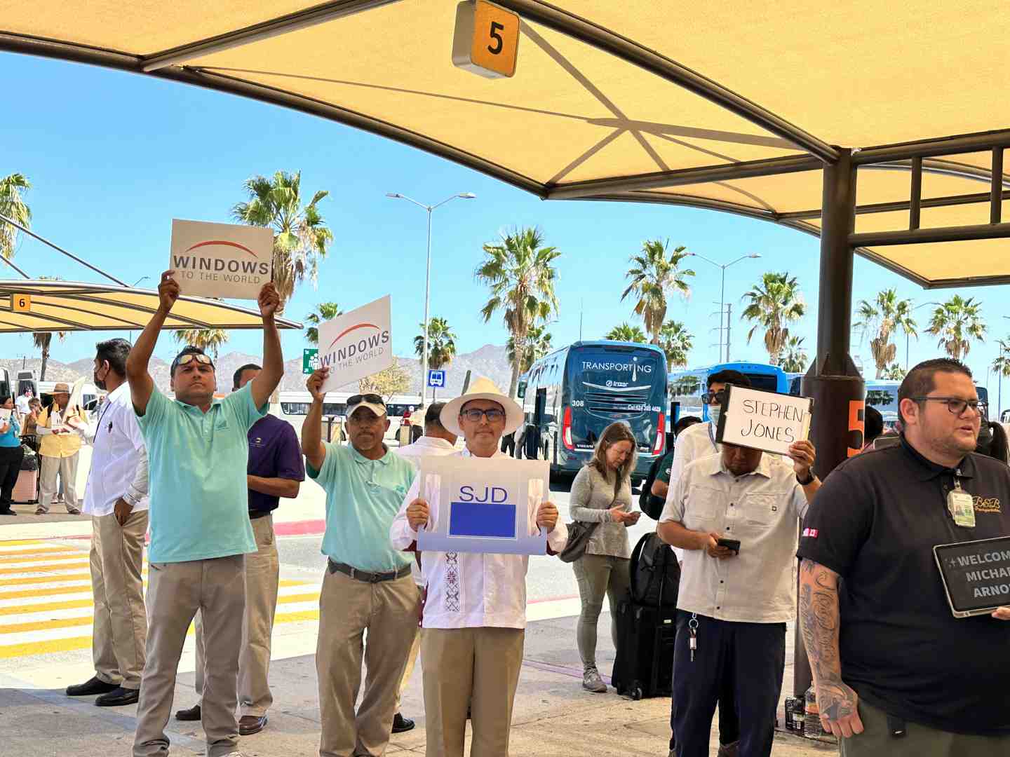 A friendly driver stands holding a sign with a guest's name, ready to greet them at the airport exit. - secrets cabo transportation