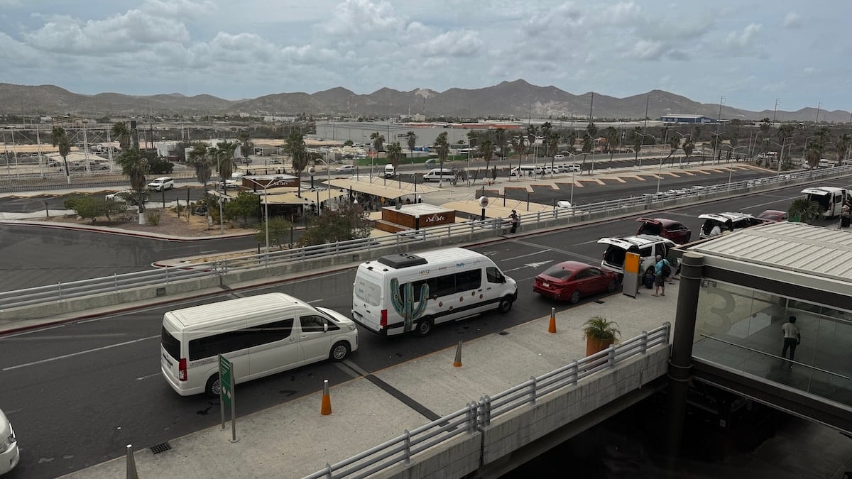 Shuttle vans and transfer vehicles lined up at the curbside pickup area outside Los Cabos International Airport